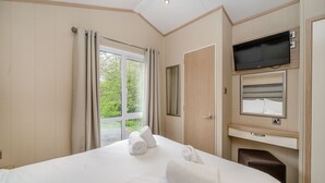 Una habitación de hotel con cama, televisión, espejo y ventana con cortinas.