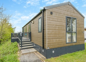 A single-story mobile home with a front porch, a small set of steps leading to the entrance, and a clear sky in the background.