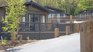 A modern cabin with a deck, surrounded by trees and a fence. - 2 bedroom accommodation in Wootton Bridge, Nr Cowes (Wootton Bridge, Nr Cowes)