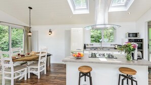 A modern kitchen with a central island, white cabinetry, and a dining area with a wooden table and white chairs. - 2 bedroom accommodation in Wootton Bridge, Nr Cowes (Wootton Bridge, Nr Cowes)