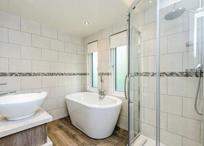 A modern bathroom with a freestanding bathtub, a glass-enclosed shower, and a large window.