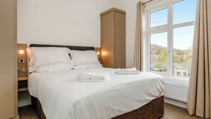 A hotel room with a large bed, a nightstand, a built-in wardrobe, and a window with curtains. - 3 bedroom accommodation in Cheddar (Cheddar)