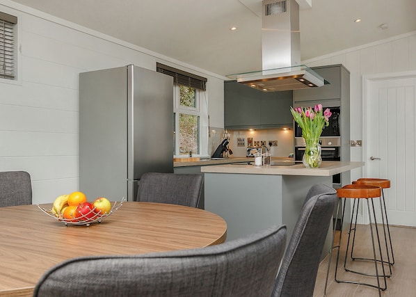 A modern kitchen with a central island, grey cabinetry, and a dining area with a round table and grey chairs.