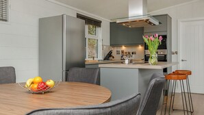 A modern kitchen with a central island, grey cabinetry, and a dining area with a round table and grey chairs. - 3 bedroom accommodation in Cheddar (Cheddar)