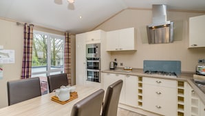 A compact kitchen with a dining area, featuring a stove, oven, microwave, and a view of the outside. - 1 bedroom accommodation in Bewaldeth, Keswick (Bewaldeth, Keswick)