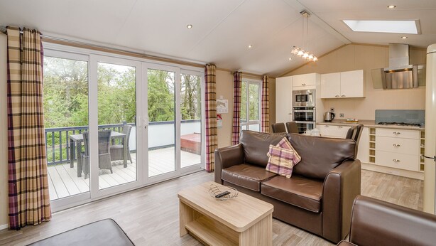 A modern living room with a brown leather sofa, a wooden coffee table, and a balcony with wicker furniture. - 1 bedroom accommodation in Bewaldeth, Keswick (Bewaldeth, Keswick)