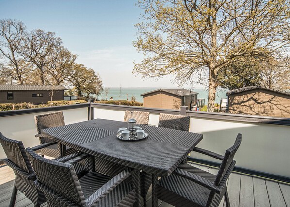 Eine Terrasse mit Tisch und Stühlen mit Blick auf ein Gewässer und Bäume.