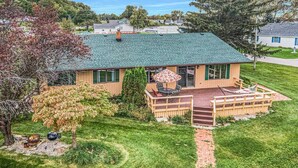A single-story house with a green roof, a front porch with a table and chairs, and a small deck. - 4B Lakefront home off M22 with access to Lake Michigan! (Onekama)