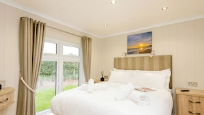 A hotel room with a large bed, a bedside table, a nightstand, a window with curtains, and a painting on the wall.
