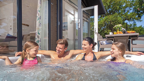 A family in a hot tub with a glass-enclosed house in the background.