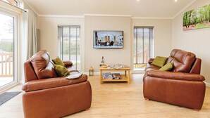 A spacious living room with two leather sofas, a coffee table, and a flat-screen TV mounted on the wall.