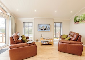A spacious living room with two leather sofas, a coffee table, and a flat-screen TV mounted on the wall.
