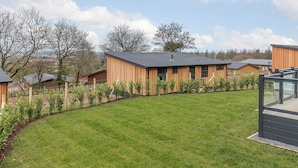 A residential area with wooden houses, a well-maintained lawn, and a clear sky. - 4 bedroom accommodation in Cheddar (Cheddar)