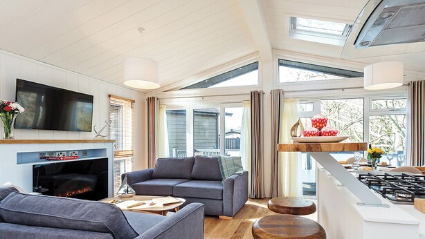A modern living room with a fireplace, grey sofas, a TV, and a kitchen area with a stove. - 2 bedroom accommodation in Wootton Bridge, Nr Cowes (Wootton Bridge, Nr Cowes)