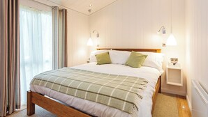 A bedroom with a wooden bed, two bedside tables, a window with curtains, and wall-mounted lights. - 2 bedroom accommodation in Wootton Bridge, Nr Cowes (Wootton Bridge, Nr Cowes)