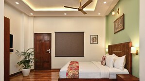 A bedroom with a wooden bed, a ceiling fan, a potted plant, and a large window. - Hotel Sethi Legacy (Haridwar)