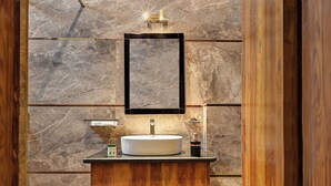 A bathroom with a marble wall, a wooden vanity, a round sink, a mirror, and a light fixture. - Hotel Sethi Legacy (Haridwar)
