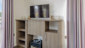 A room with a flat-screen TV mounted on a wooden shelf above a fireplace, flanked by striped curtains. - 4 bedroom accommodation in Wootton Bridge, Nr Cowes (Wootton Bridge, Nr Cowes)