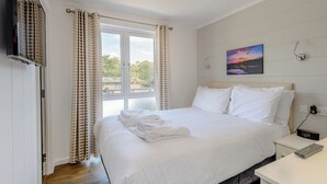 A bedroom with a bed, curtains, a painting, a TV, and a bedside table. - 4 bedroom accommodation in Wootton Bridge, Nr Cowes (Wootton Bridge, Nr Cowes)
