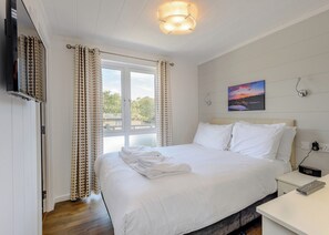 Makuuhuone, jossa on sänky, verhot, taulu, televisio ja yöpöytä.