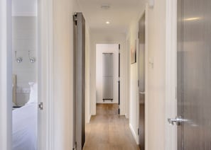 Un couloir avec un plancher en bois, des murs blancs et une porte sur le côté droit.