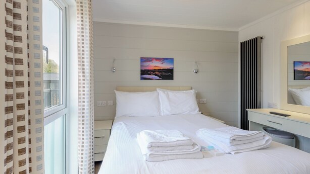 A hotel room with a bed, a bedside table, a mirror, and a window with curtains. - 4 bedroom accommodation in Wootton Bridge, Nr Cowes (Wootton Bridge, Nr Cowes)