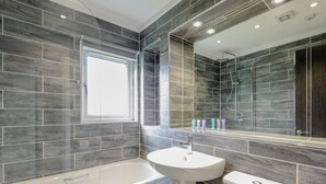 A modern bathroom with a bathtub, sink, and toilet, featuring dark grey tiles and a large mirror. - 4 bedroom accommodation in Wootton Bridge, Nr Cowes (Wootton Bridge, Nr Cowes)