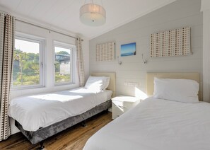 Une chambre avec deux lits, une fenêtre, une table de chevet et un luminaire fixé au mur.