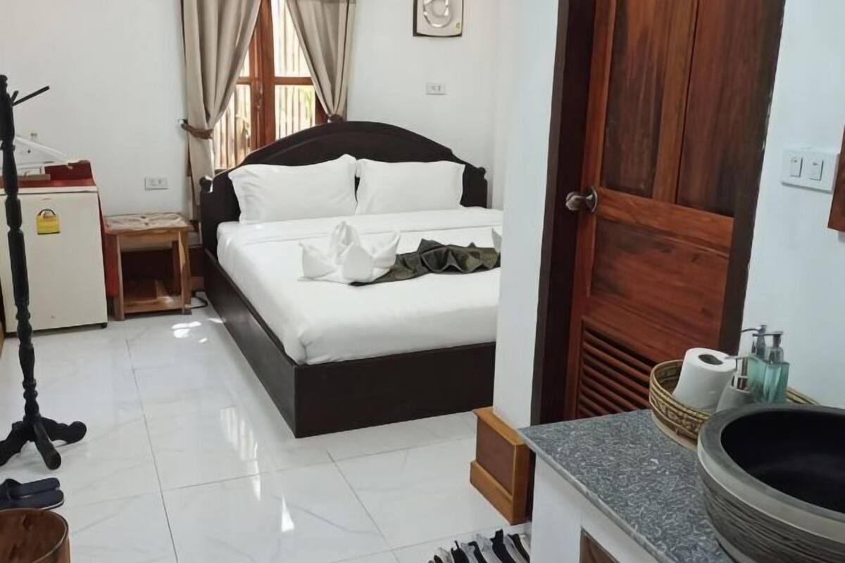 A bedroom with a bed, a desk, a chair, a lamp, a sink, and a window.