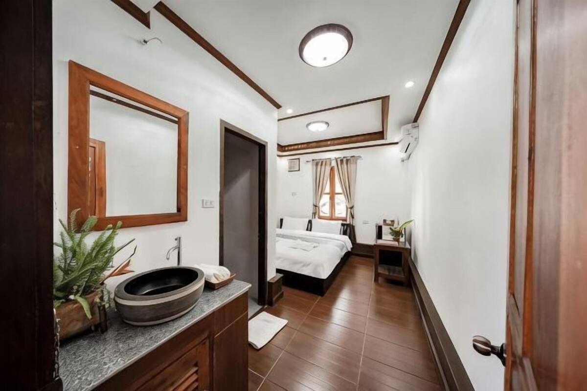 A hotel room with a wooden vanity, a large mirror, a bed with white bedding, a bedside table, and a window with curtains.