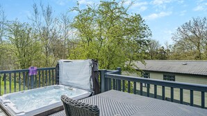 A hot tub on a wooden deck with wicker furniture, surrounded by trees and a house in the background. - Wordsworth Premier Select (Bewaldeth, Keswick)