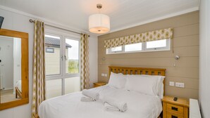 A bedroom with a large bed, a bedside table, a nightstand, a mirror, a window with curtains, and a ceiling light. - Wordsworth Premier Select (Bewaldeth, Keswick)