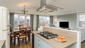 Una cocina moderna con una isla central, un comedor con sillas de madera, una araña y un televisor.