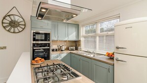 Una cocina moderna con estufa a gas, hornos empotrados, refrigerador y un amplio ventanal con persianas.
