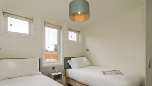 Un dormitorio con dos camas, una ventana, una mesita de noche y una lámpara colgante.