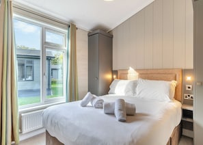 A hotel room with a large bed, a window with curtains, a radiator, and a wall-mounted light. - Bakewell Premier Lodge (Ashbourne)
