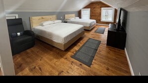 A bedroom with a large bed, a small sofa, a TV, and wooden flooring.