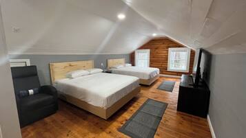 A bedroom with a large bed, a small sofa, a TV, and wooden flooring.