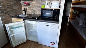 Una cocina compacta con armarios de madera, un microondas, un refrigerador pequeño y un lavamanos.
