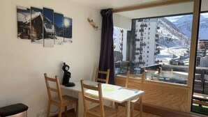 Una habitación con una mesa y sillas de madera, un pequeño calentador y vistas a un pueblo nevado a través de amplios ventanales.