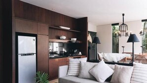 A modern kitchen with a built-in refrigerator, wooden cabinets, and a dining area with a sofa and table. - Villa Ambergris by Nakula (Nusa Dua)