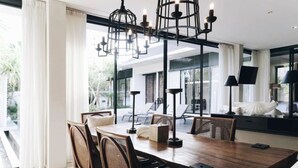 A modern dining area with a wooden table, wicker chairs, and pendant lighting. - Villa Ambergris by Nakula (Nusa Dua)