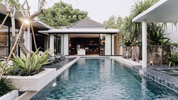 A modern house with a swimming pool, outdoor seating, and a stone wall. - Villa Ambergris by Nakula (Nusa Dua)
