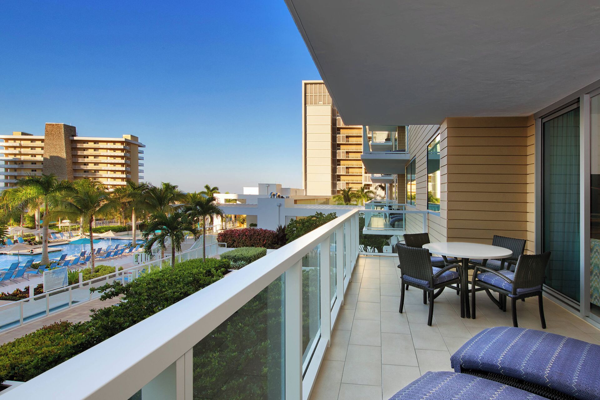 Un balcon avec vue sur la piscine, un espace salon extérieur et un panorama sur la ville en arrière-plan.