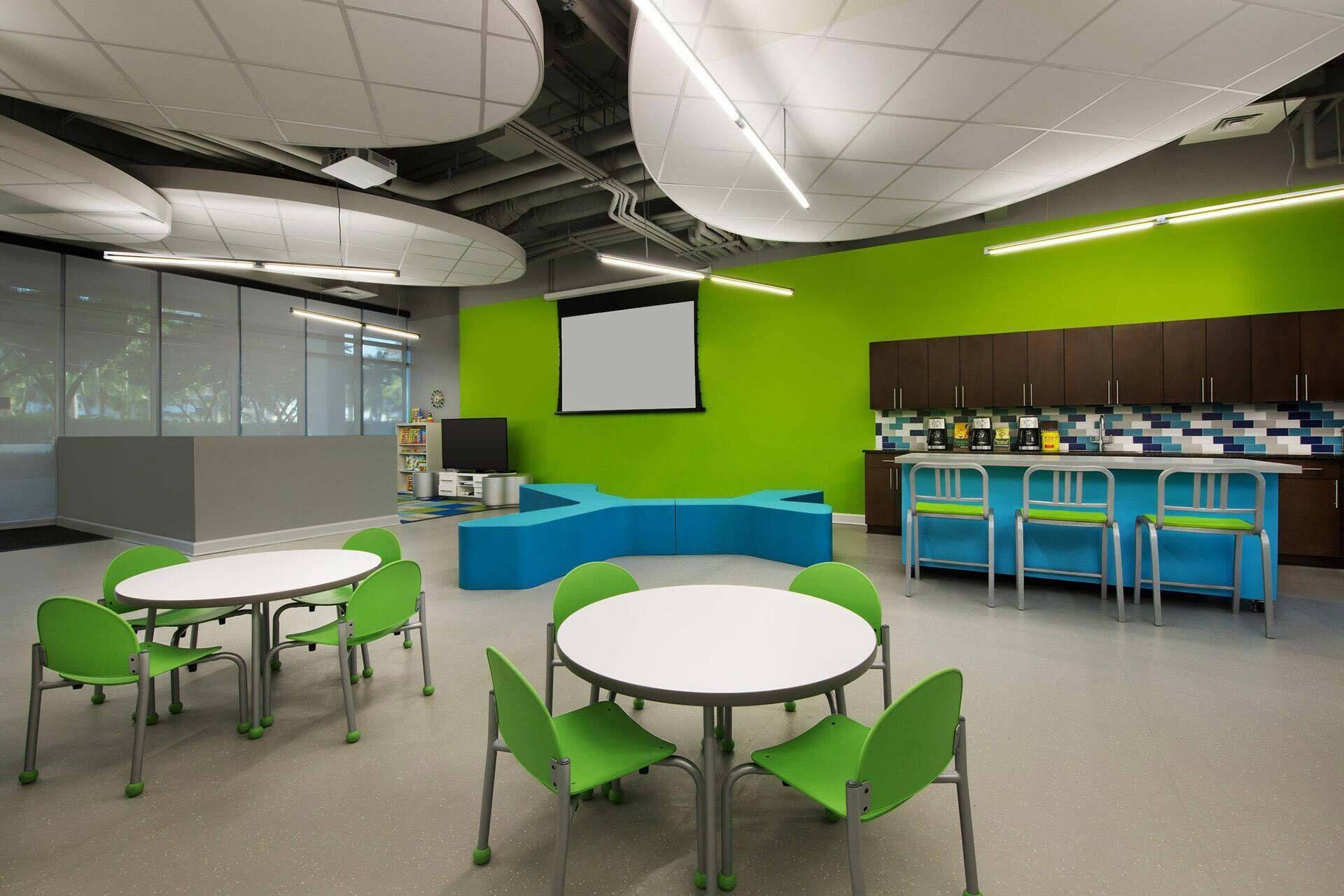 A modern indoor space with a green wall, a white screen, and a bar area.