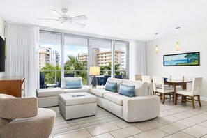 Relax in a spacious room with a sofa, dining table, and flat-screen TV, offering a view of the surrounding buildings and palm trees.