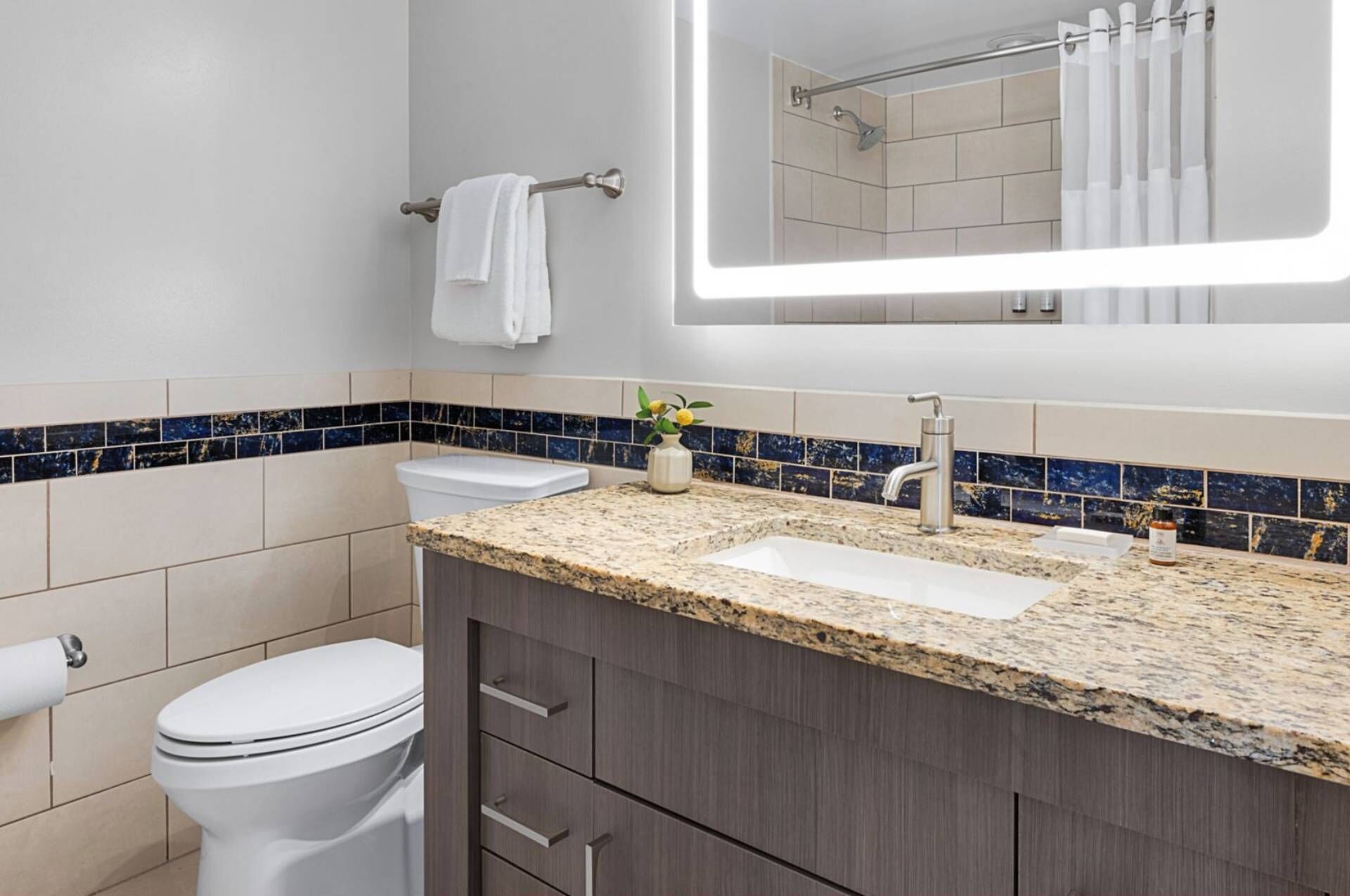 Une salle de bain moderne avec des toilettes blanches, un lavabo doté d’un plan de travail en marbre et un miroir au-dessus du lavabo.