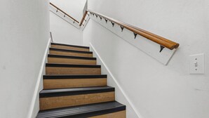 A staircase with wooden steps and a handrail, white walls, and a light switch.