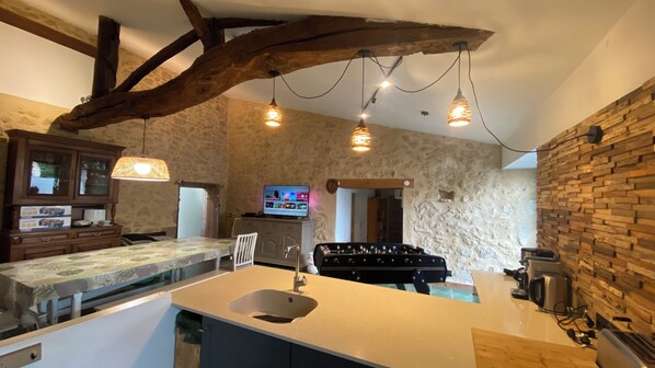 Una cocina con pared de piedra, vigas de madera, un lavamanos y una mesa de futbolín.