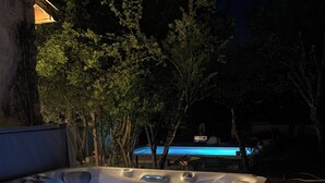 A hot tub with blue lighting, surrounded by trees and a building in the background.